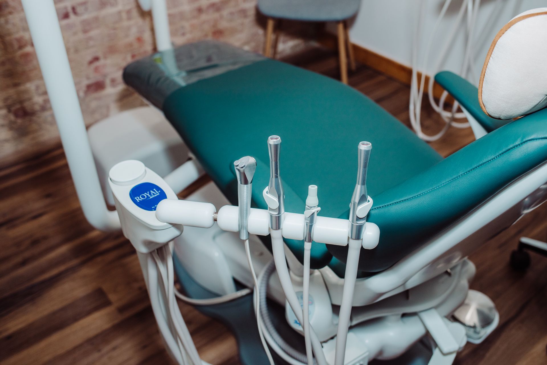 Dental chair with tools, teal upholstery, and wood floor.