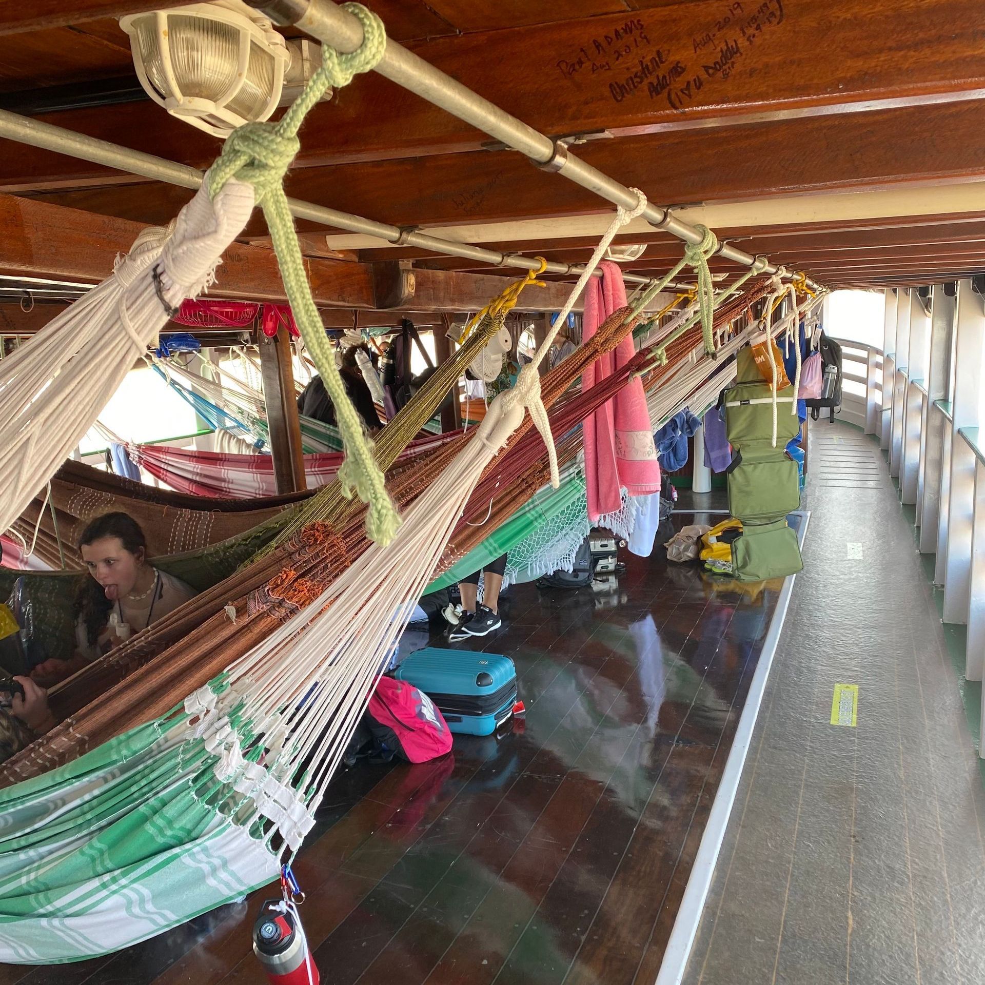 Hammocks strung on a boat deck, people lounging, luggage nearby.