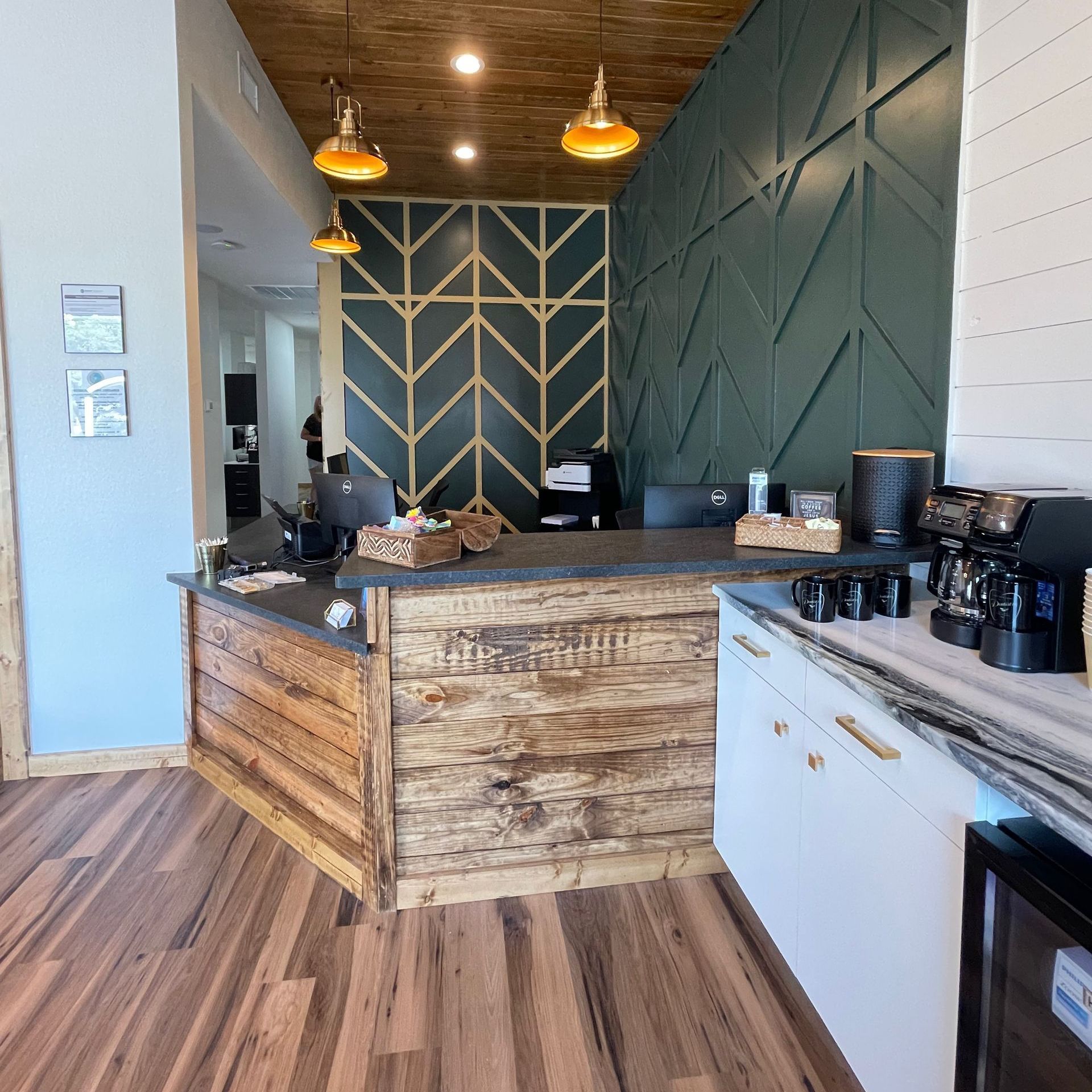 Reception area with wooden accents, teal geometric wall, and coffee station.