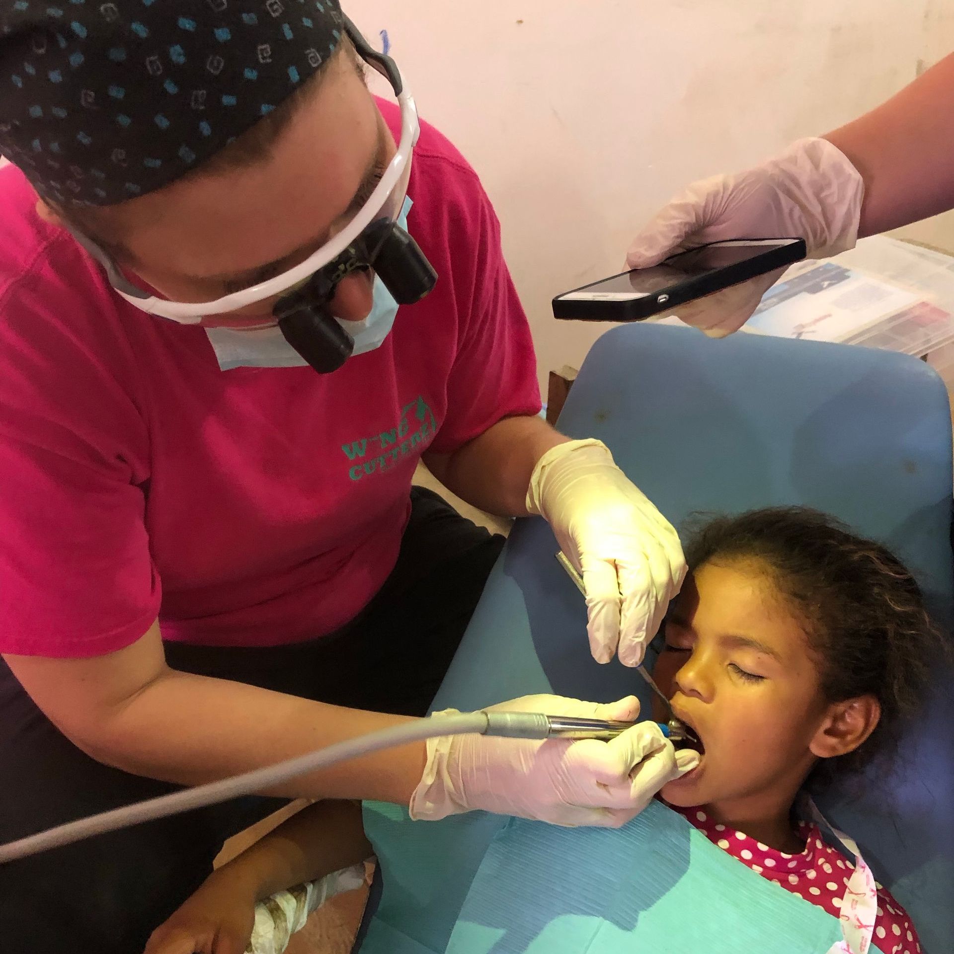 Dentist examining a child's teeth; dentist wearing magnification glasses, child in dental chair.