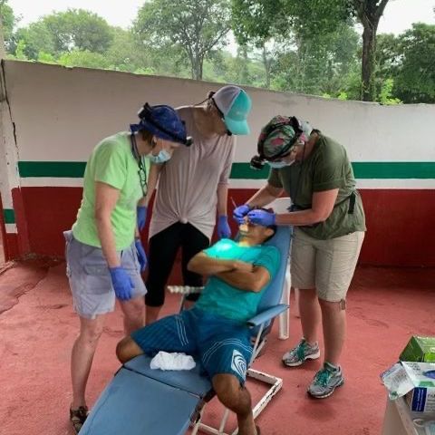 Four people providing dental care outdoors. One person reclines in a chair, receiving treatment.
