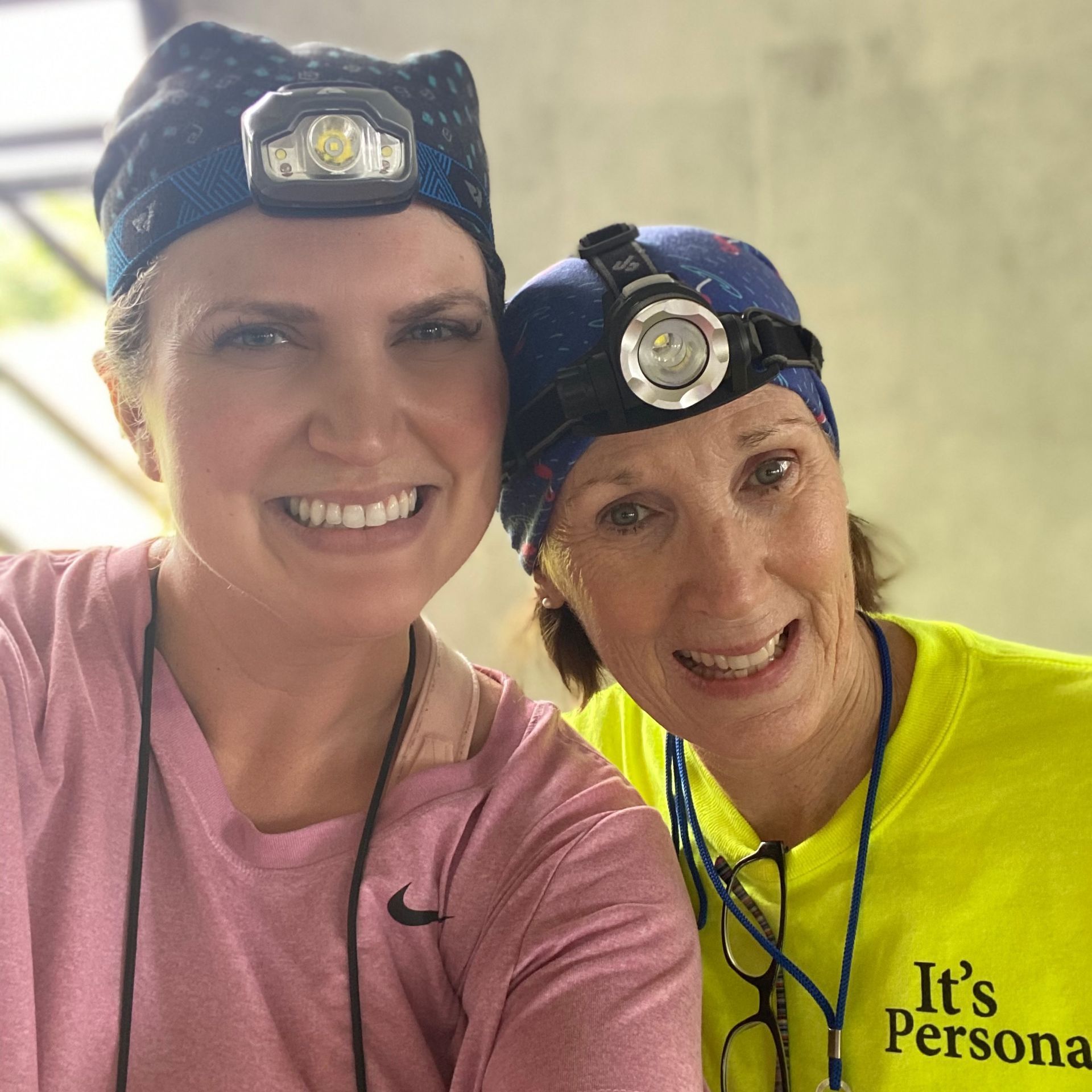 Two women smiling, wearing headlamps. One in pink shirt, other in yellow shirt.