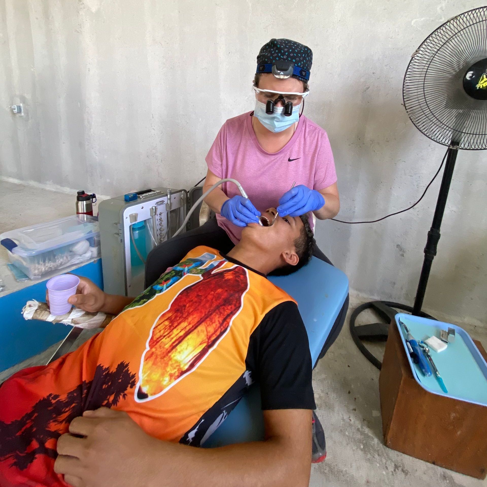 Dentist treating a patient's teeth outdoors. The patient is reclining in a dental chair.