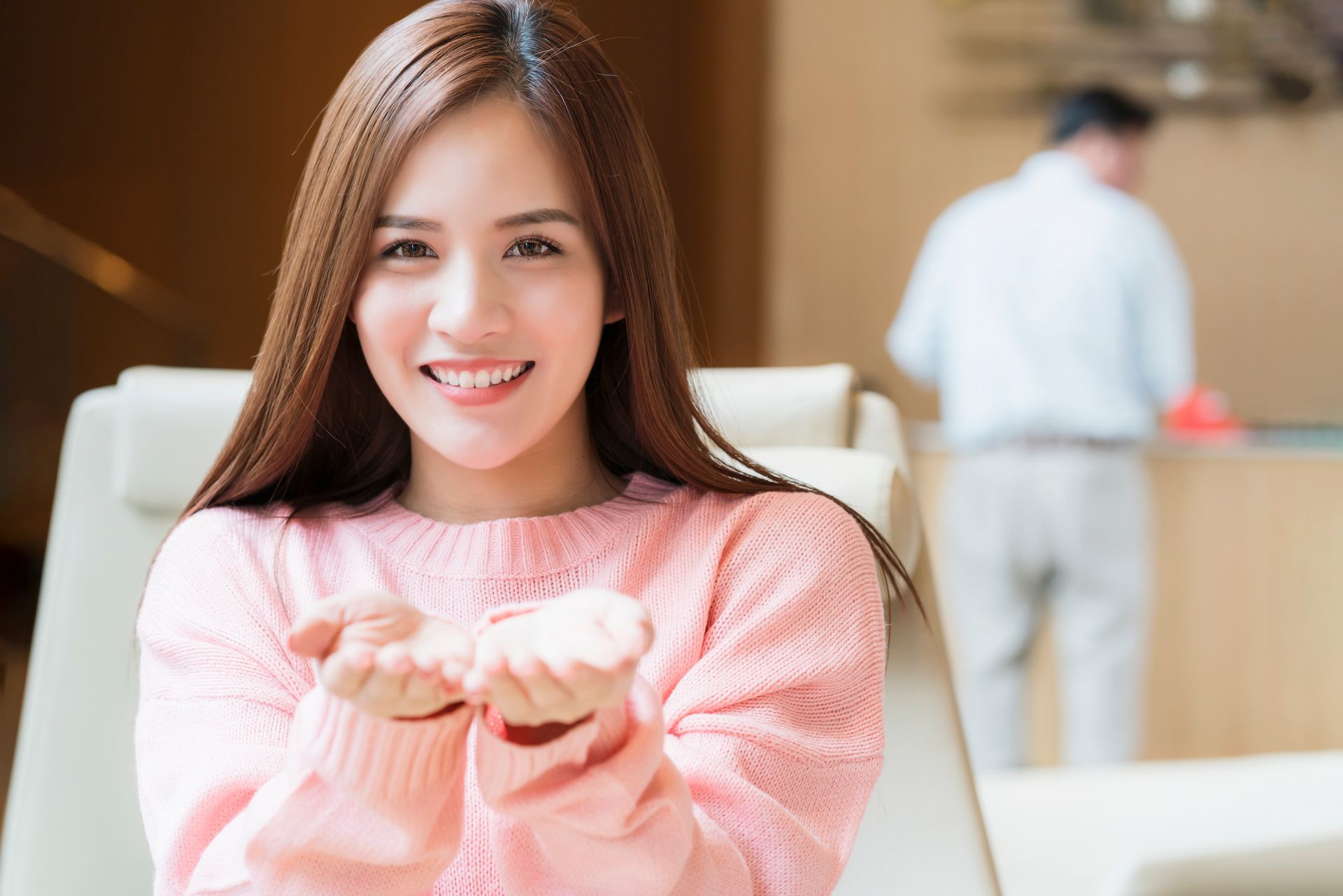 Woman in pink sweater smiling, holding out her hands, indoor setting.
