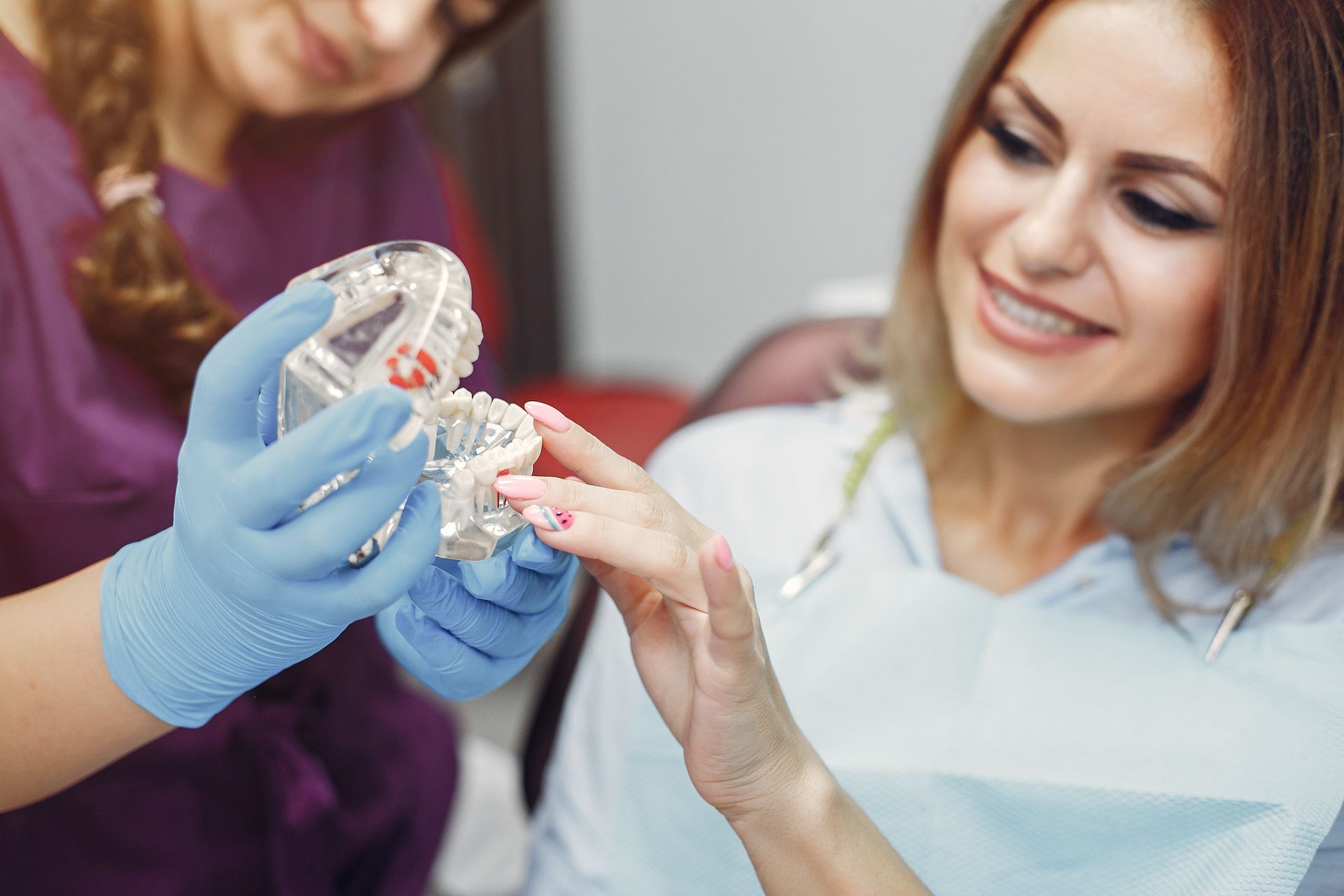 Dentist holding teeth model explains dental work to smiling patient in a clinic.