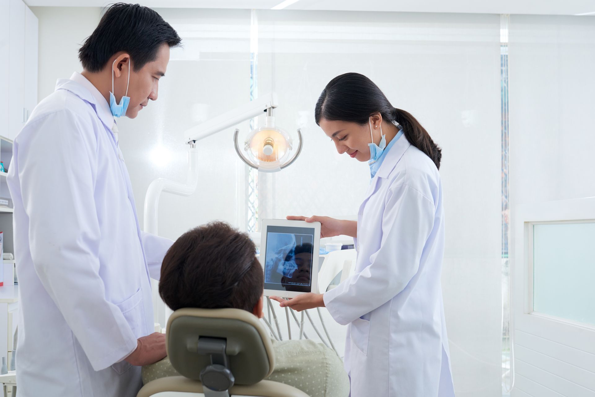 Dentist showing patient a dental x-ray on a tablet, assistant nearby, dental office setting.