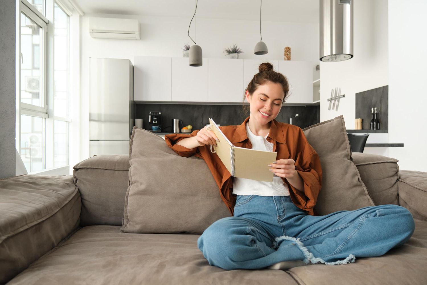 Woman sitting on a gray couch reading a letter in a bright living room
