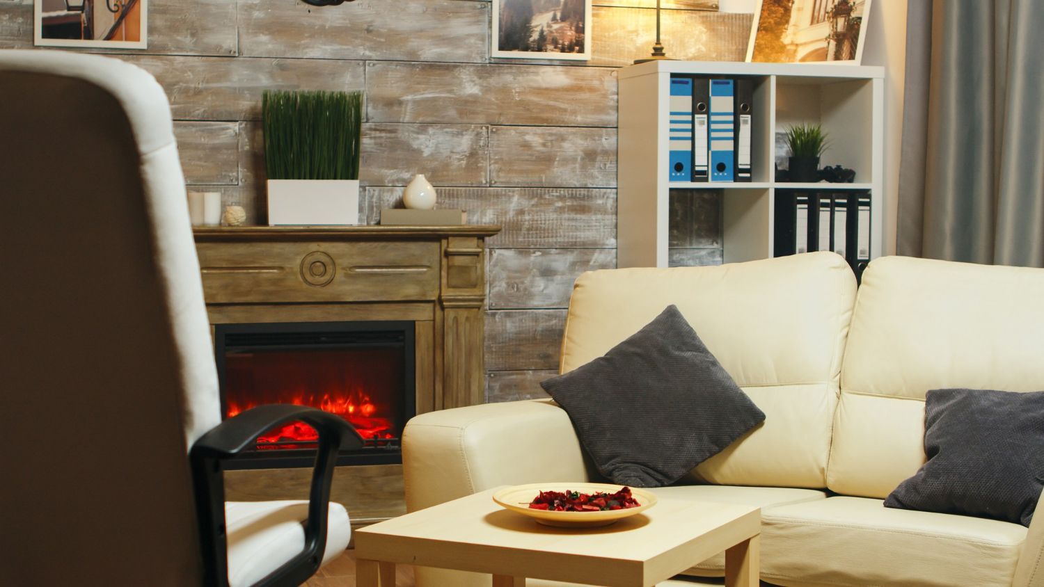 Cozy living room with cream sofa, fireplace, wooden table, and shelving unit against a stone wall.