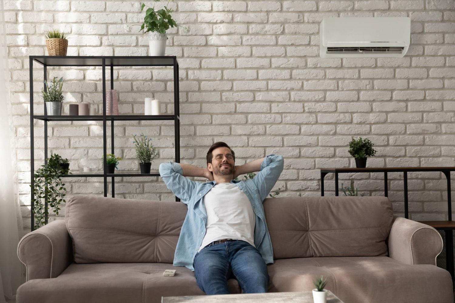 Person reclining on a sofa in a bright living room with plants and a wall-mounted air conditioner