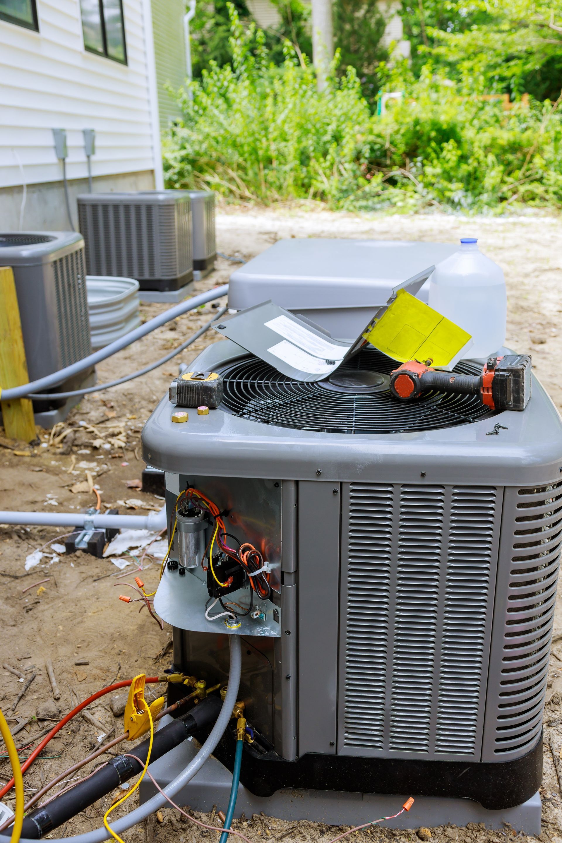 Damaged outdoor air conditioner unit with exposed wiring and tools beside a house