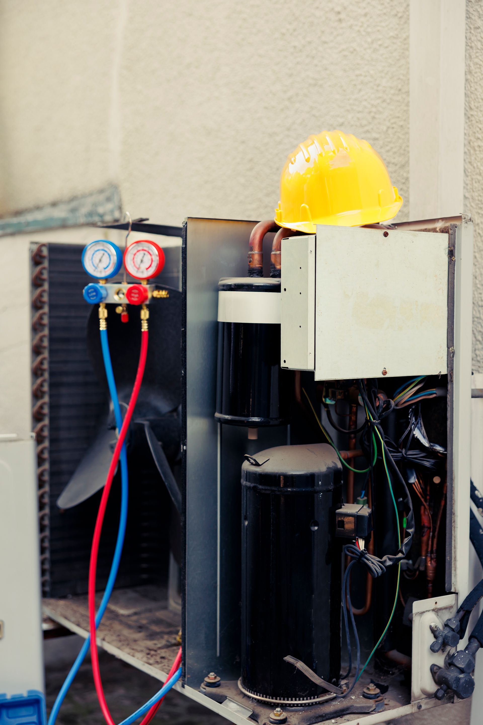 Open electrical equipment with hoses, gauges, and a yellow hard hat on top in a narrow utility area