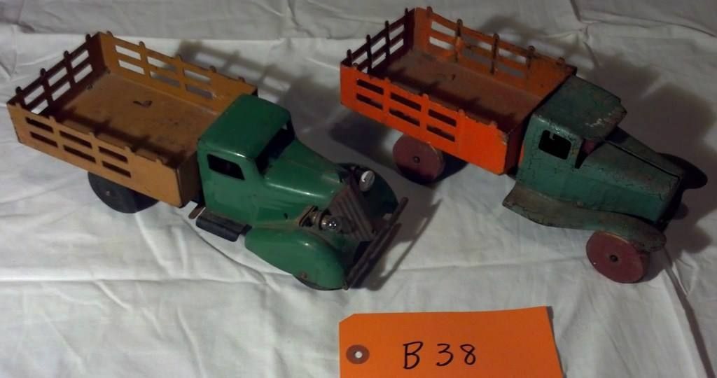 Two vintage toy trucks, green and orange, on a white cloth with a small orange tag nearby.