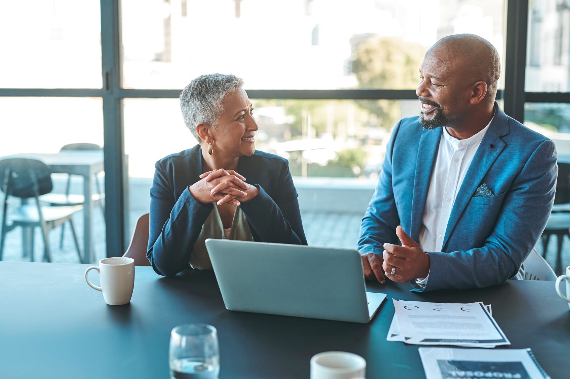 Two people talking at a table with a laptop in a bright office lounge