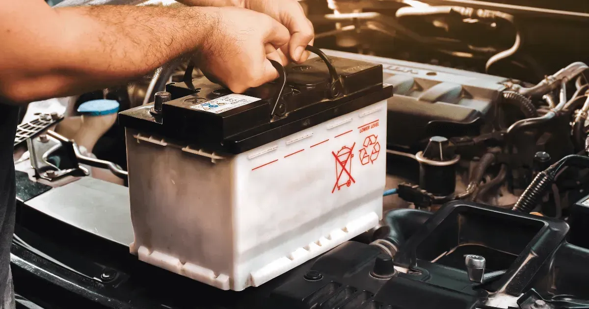 Person installing a car battery in an engine bay with a wrench