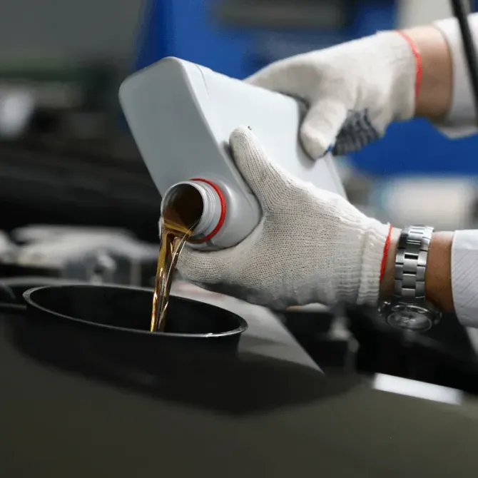 Gloved hands pour motor oil from a white container into a car engine