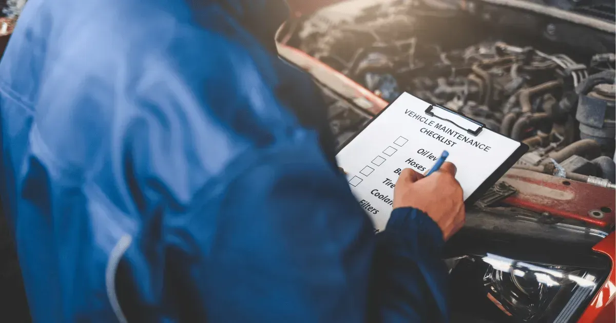 Mechanic writing on a clipboard beside an open car engine in a workshop