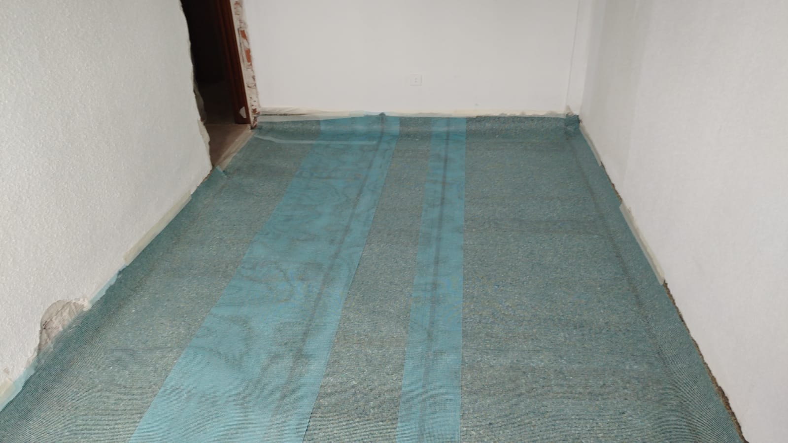 Una habitación con una alfombra azul en el suelo y una pared blanca.
