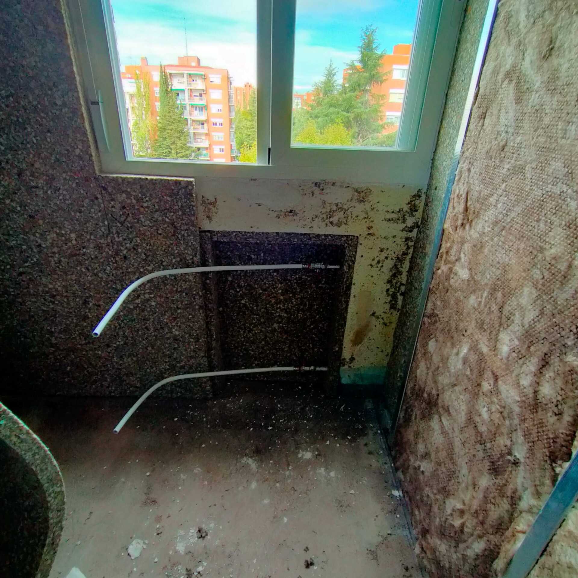 Una habitación sucia con una ventana y un edificio de ladrillo al fondo