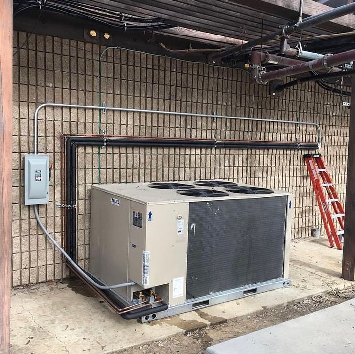 A large air conditioner is sitting outside of a building next to a ladder.
