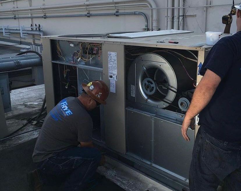 Two men are working on an air conditioner on the roof of a building.
