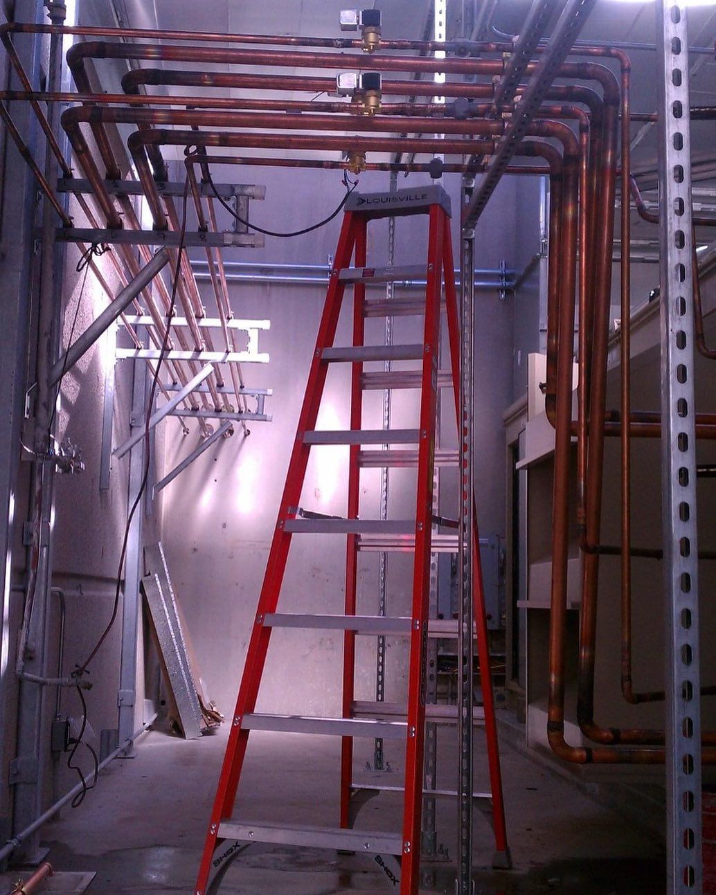 A red ladder in a room with copper pipes