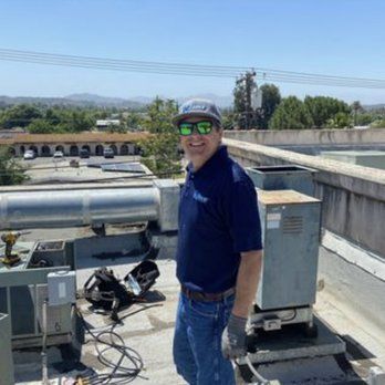 A man wearing sunglasses and a hat is standing on top of a roof.
