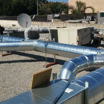 A satellite dish is sitting on top of a building next to a bunch of metal pipes.