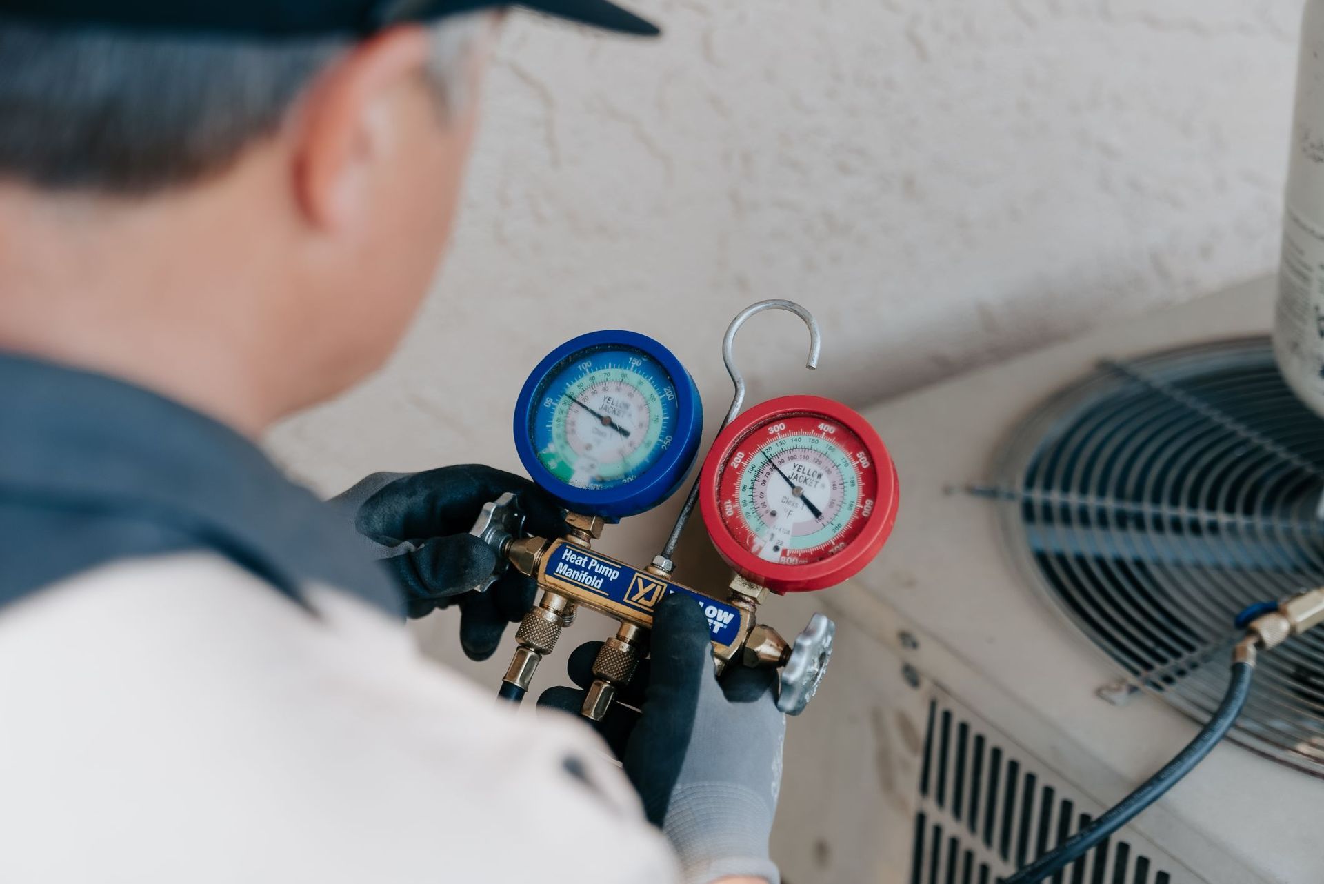 A man is working on an air conditioner with two gauges attached to it.