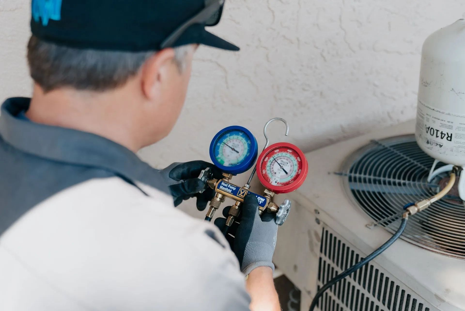 Technician connecting gauges to an outdoor air conditioner unit for maintenance
