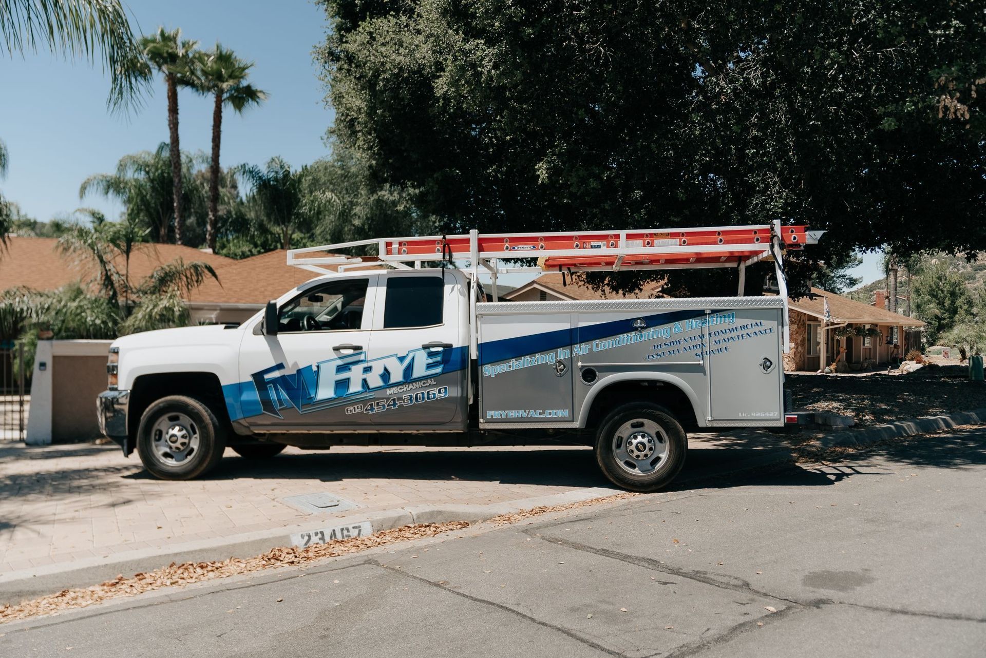 A white truck with a ladder on top of it is parked on the side of the road.