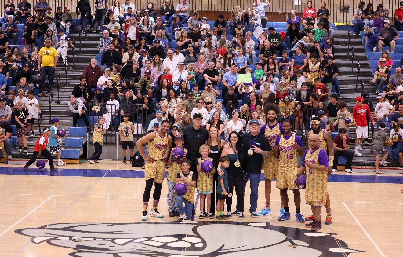 Basketball team posing on court with cheerleaders and crowd in the stands behind them