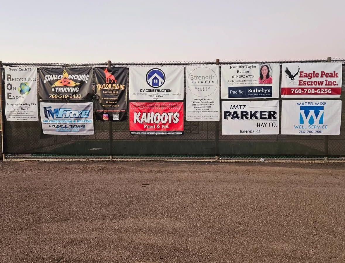 Sponsor banners on a chain-link fence above a gravel field under a cloudy sky