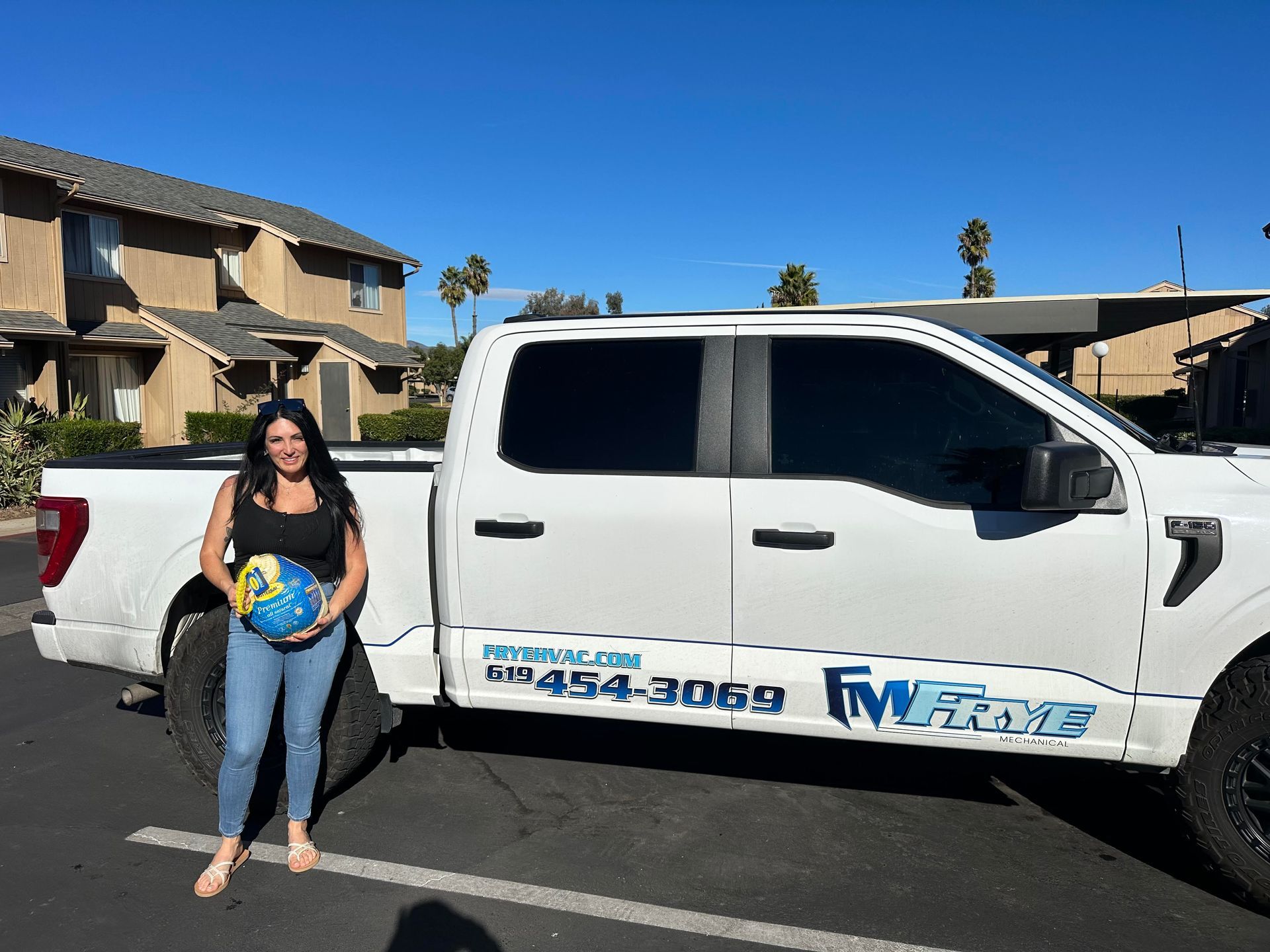 Woman standing beside a white pickup truck with company branding in a residential neighborhood.