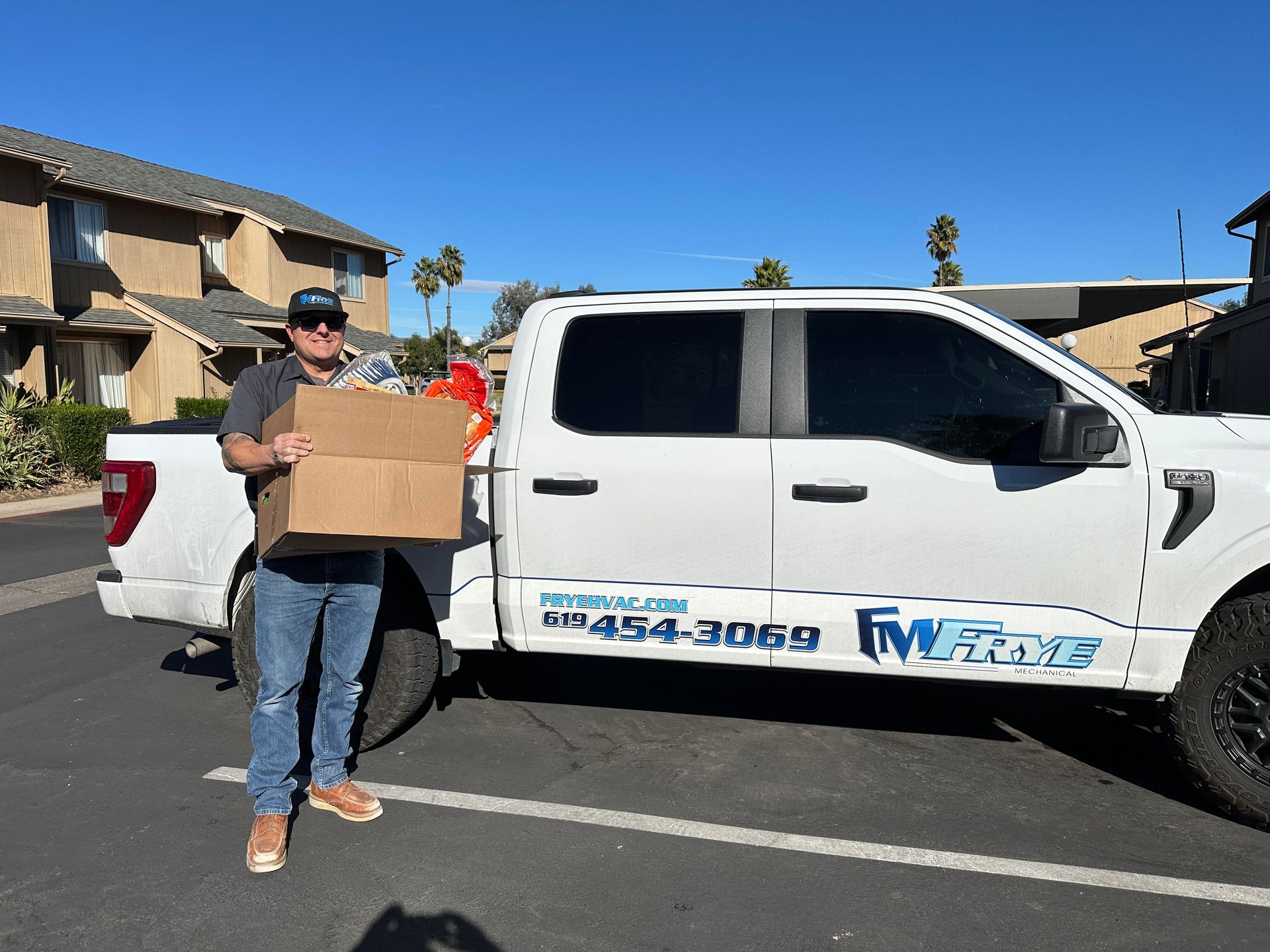 Man holding a cardboard box beside a white pickup truck in a sunny residential street