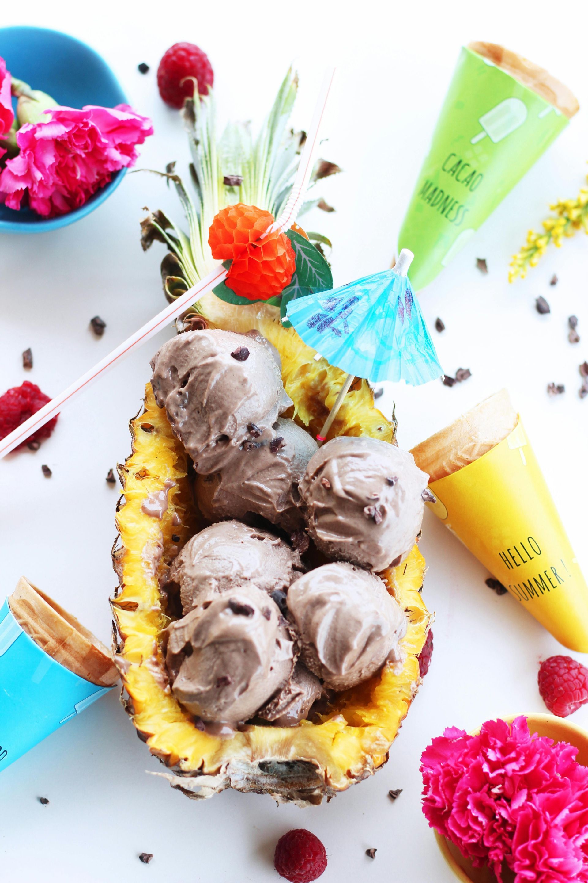 Chocolate ice cream scoops in a carved pineapple, with cones, berries, and cocktail umbrellas.