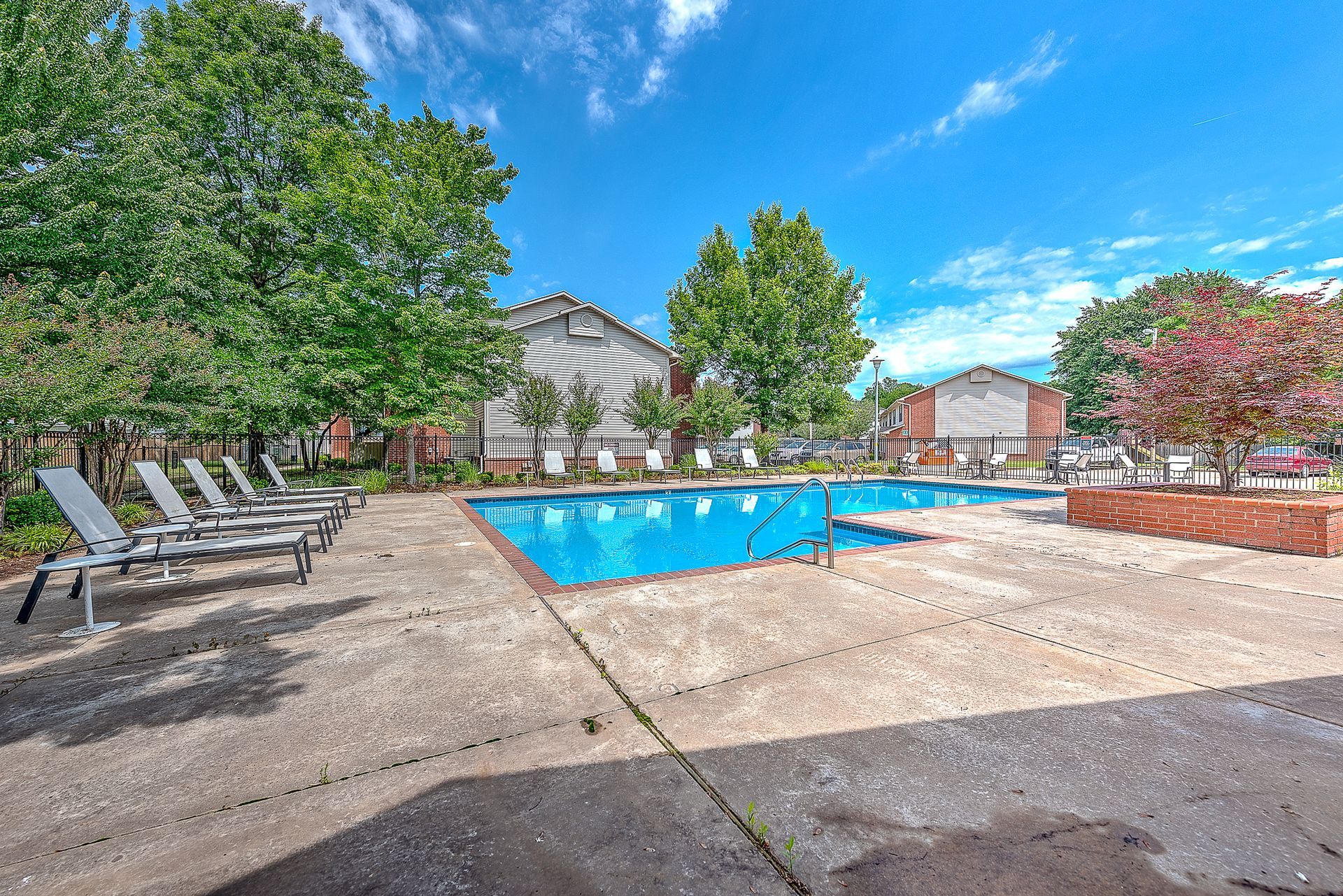 A large swimming pool is surrounded by chairs and trees.