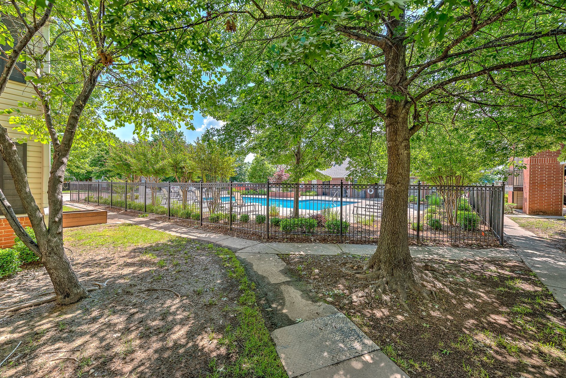A fenced in yard with trees and a pool in the background.