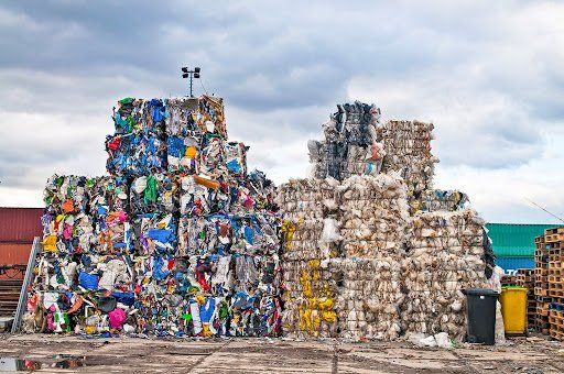 A large pile of recycling waste is sitting on top of a dirt field.