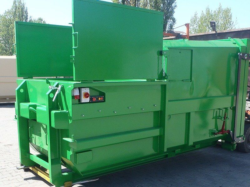 A green dumpster with the door open is parked on the side of the road.