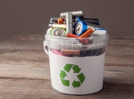 A recycling bin filled with batteries and cans on a wooden table.