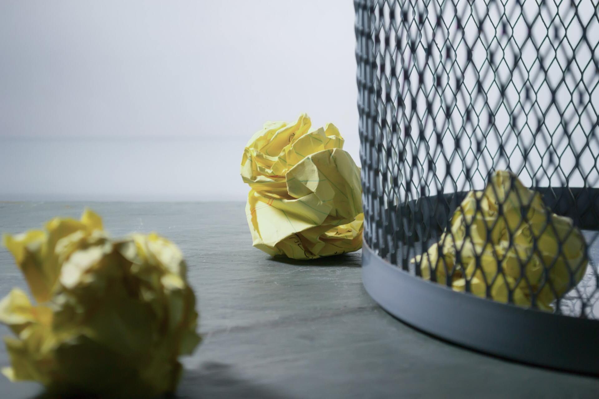 Two crumpled pieces of paper are sitting on a table next to a trash can.