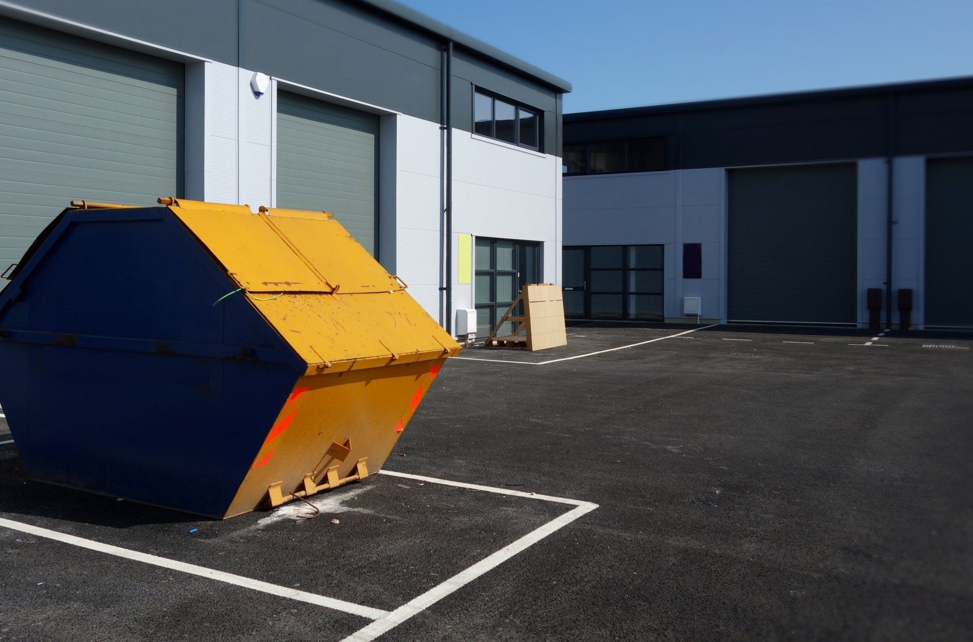 A yellow dumpster is in a parking lot in front of a building