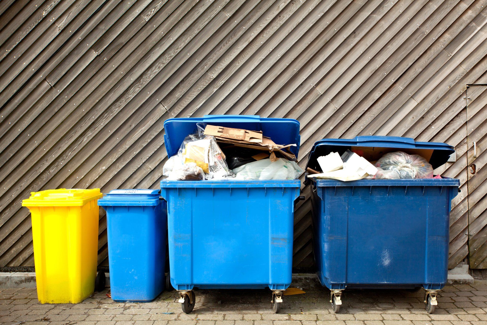 Three trash cans are lined up in front of a wooden wall.
