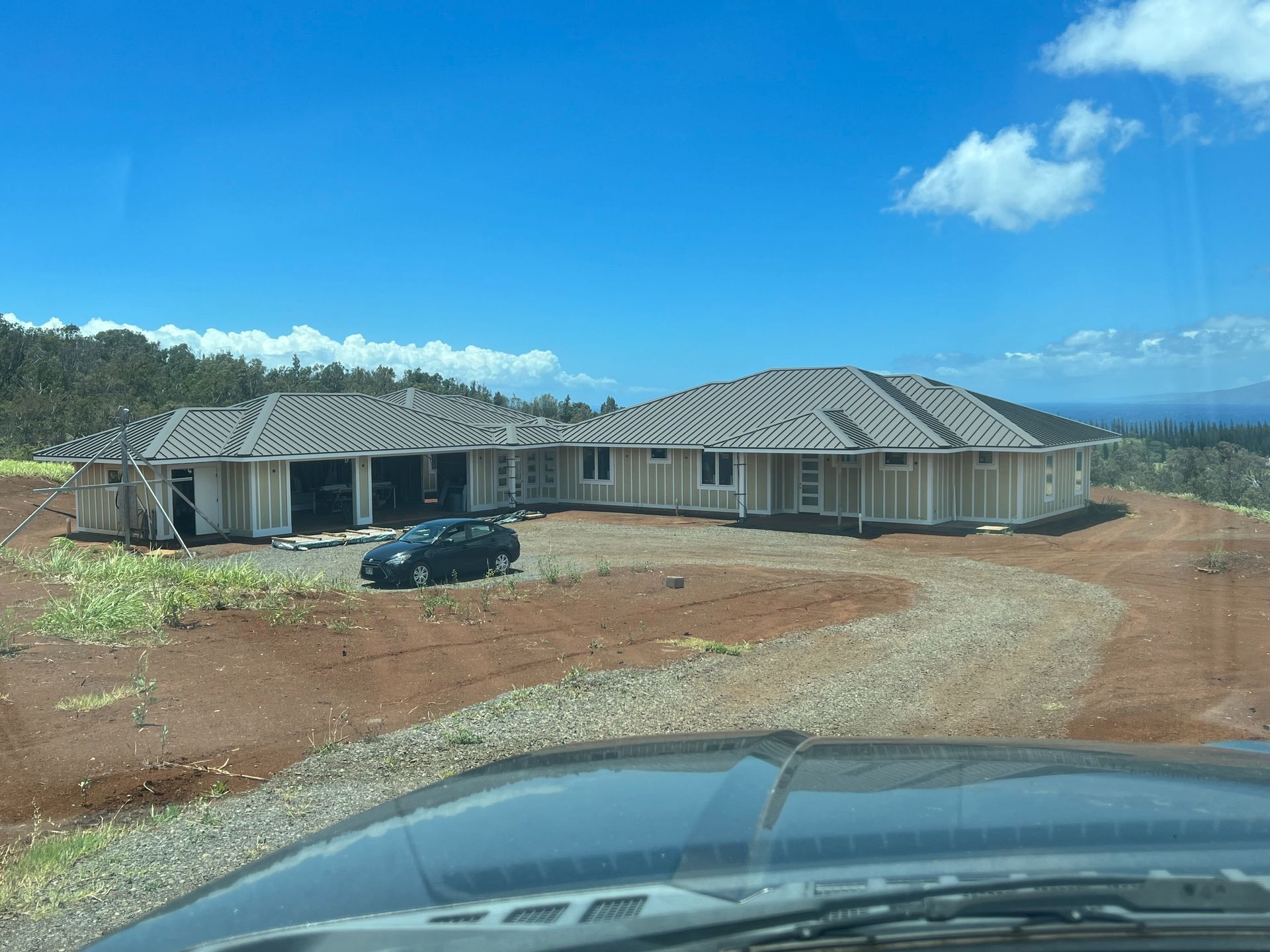 New house under construction on a red dirt lot, with a car in front and blue sky overhead