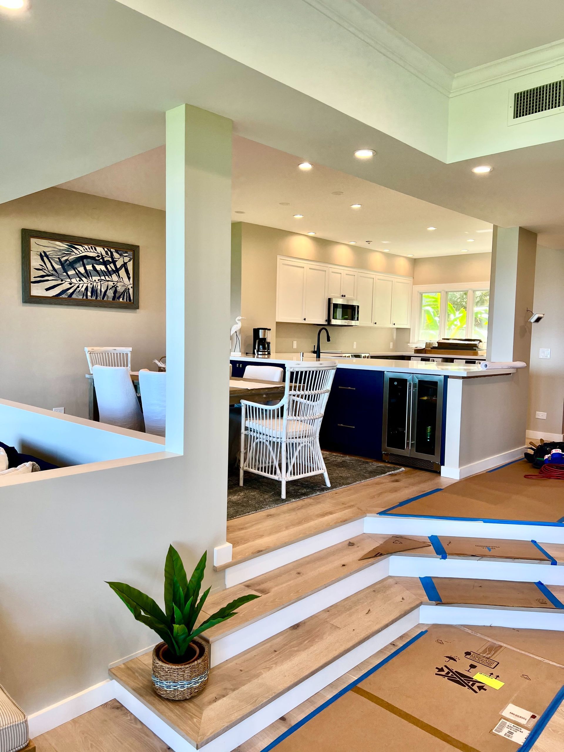 Open-plan kitchen and dining area with white cabinets, black stools, and a small plant by steps.
