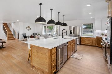 Modern kitchen with large island, wood cabinets, black pendant lights, and staircase in the background