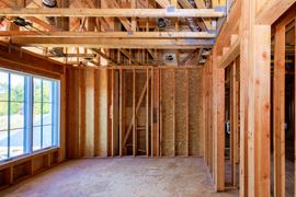Framed wooden house interior with exposed beams, studs, and large windows in daylight