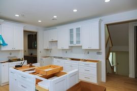 Bright white kitchen with island, wood countertops, cabinets, and doorway to stairs.