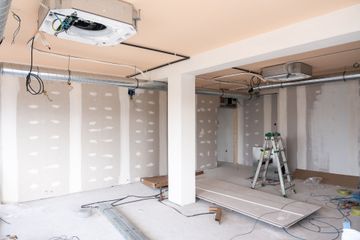 Unfinished garage interior with drywall, exposed ceiling wiring, and a ladder on the floor