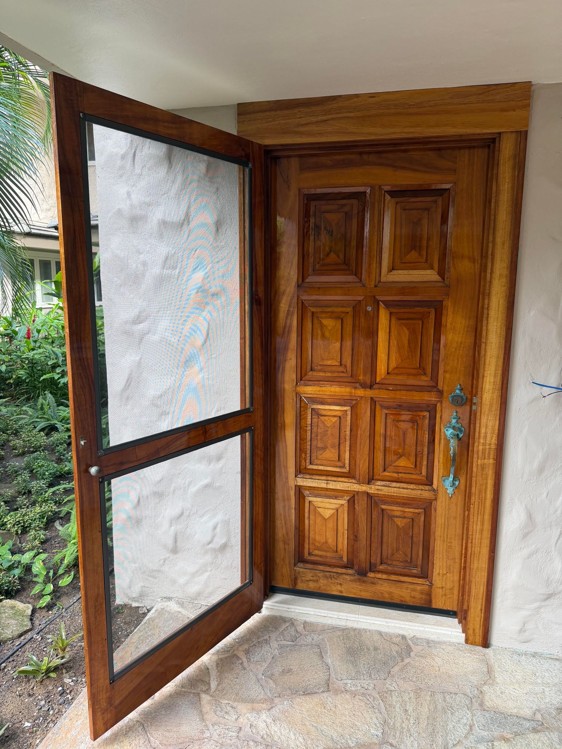 Open wooden front door with frosted glass side panel and blue handle in a porch entrance